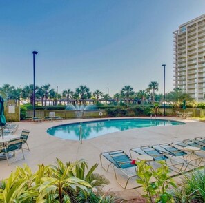 Relax by the resort pool surrounded by lush greenery and lounge chairs.