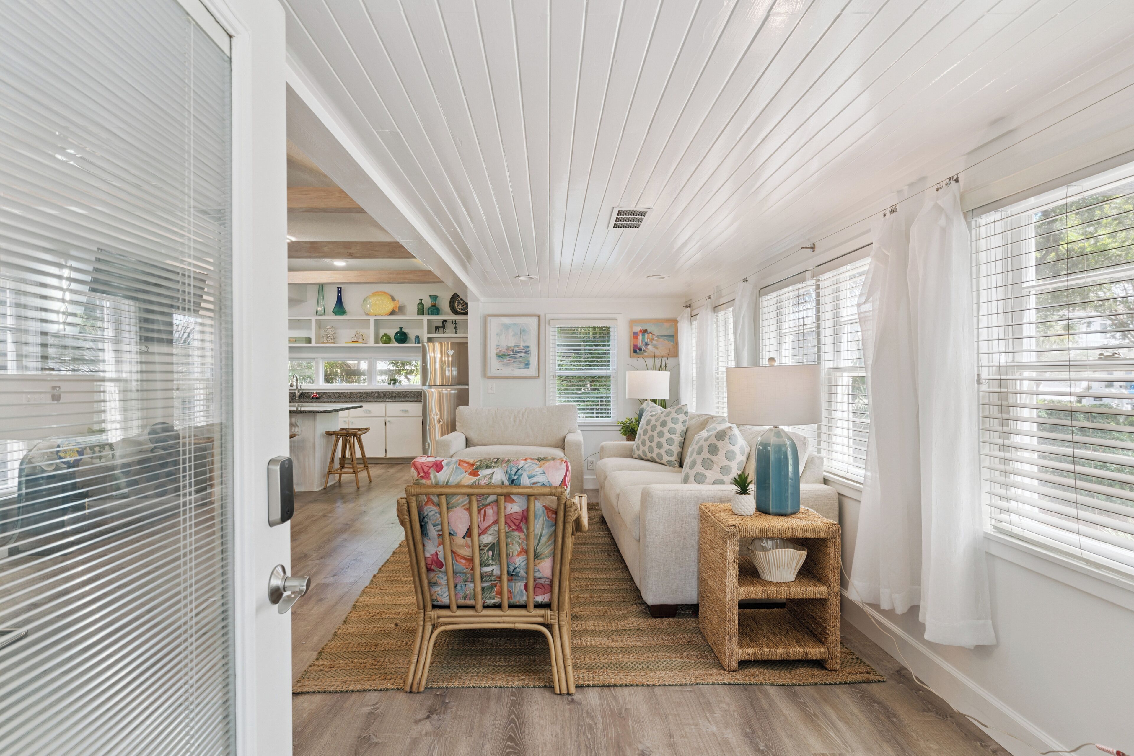 A spacious living area with a kitchen in the background, a wicker chair, and a sofa.