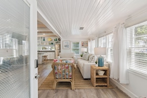 A spacious living area with a kitchen in the background, a wicker chair, and a sofa.