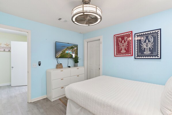A bedroom with a bed, a dresser, a ceiling fan, and two framed pictures on the wall.