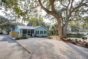 A house with a blue exterior, a gravel driveway, and a large tree in front.
