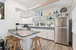 A modern kitchen with a central island, stainless steel appliances, and a view of the outdoors. - One Lot off the Beach, a Sophisticated Chic East Beach Retreat w Heated Pool (Saint Simons Island)