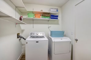 A laundry room with a washing machine, dryer, shelves with baskets, and a box labeled 'Classic'.