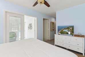 A bedroom with a bed, a dresser, a ceiling fan, a window with blinds, and a door leading to another room. - One Lot off the Beach, a Sophisticated Chic East Beach Retreat w Heated Pool (Saint Simons Island)