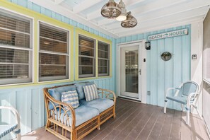 A covered porch with a wicker sofa, two chairs, and a sign reading 'BEACH HOUSE'.