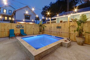 A swimming pool with a wooden deck, lounge chairs, and string lights.