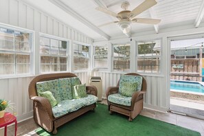 A sunroom with wicker furniture, a ceiling fan, and a view of a backyard with a pool. - One Lot off the Beach, a Sophisticated Chic East Beach Retreat w Heated Pool (Saint Simons Island)