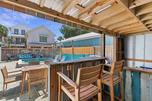 A covered outdoor area with a pool, wooden furniture, and a bar. - One Lot off the Beach, a Sophisticated Chic East Beach Retreat w Heated Pool (Saint Simons Island)