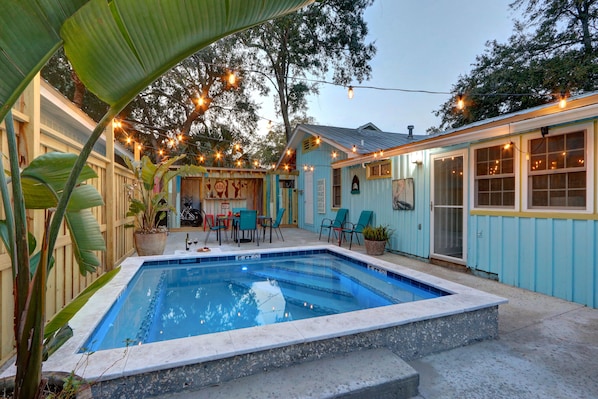 A backyard with a swimming pool, outdoor seating, and string lights.