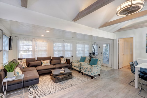 A spacious living room with a sectional sofa, patterned armchairs, a coffee table, and a dining area with a table and chairs.