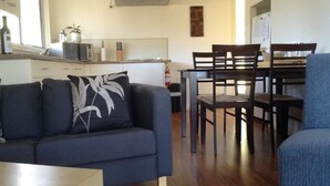 A living room with a sofa, a dining table, and chairs. There is a kitchen area in the background with a microwave and a stove. - 1 Bedroom Cottage, overlooking the Vineyard (Pokolbin)