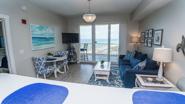 Un salon avec vue sur l’océan, un balcon et un coin repas avec des chaises à motifs bleus.