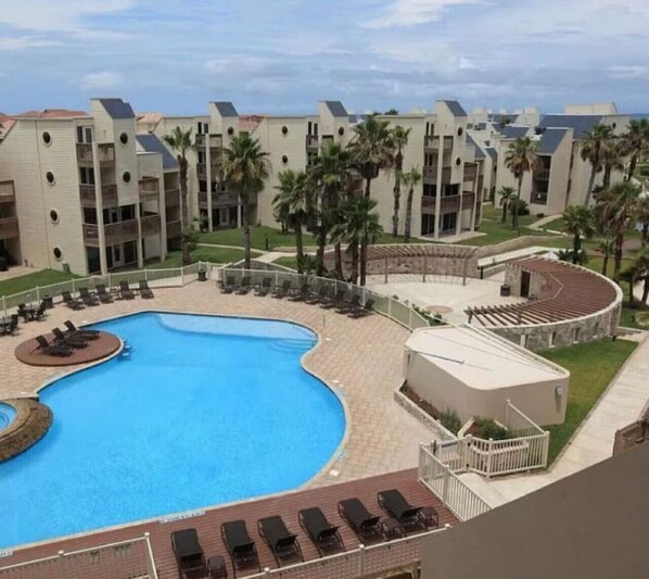 A resort with a large swimming pool, multiple balconies, and palm trees.
