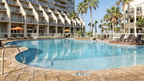 A hotel pool area with a large pool, lounge chairs, and palm trees.