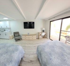 Une chambre avec deux lits, un bureau, une chaise, une télévision et un balcon.