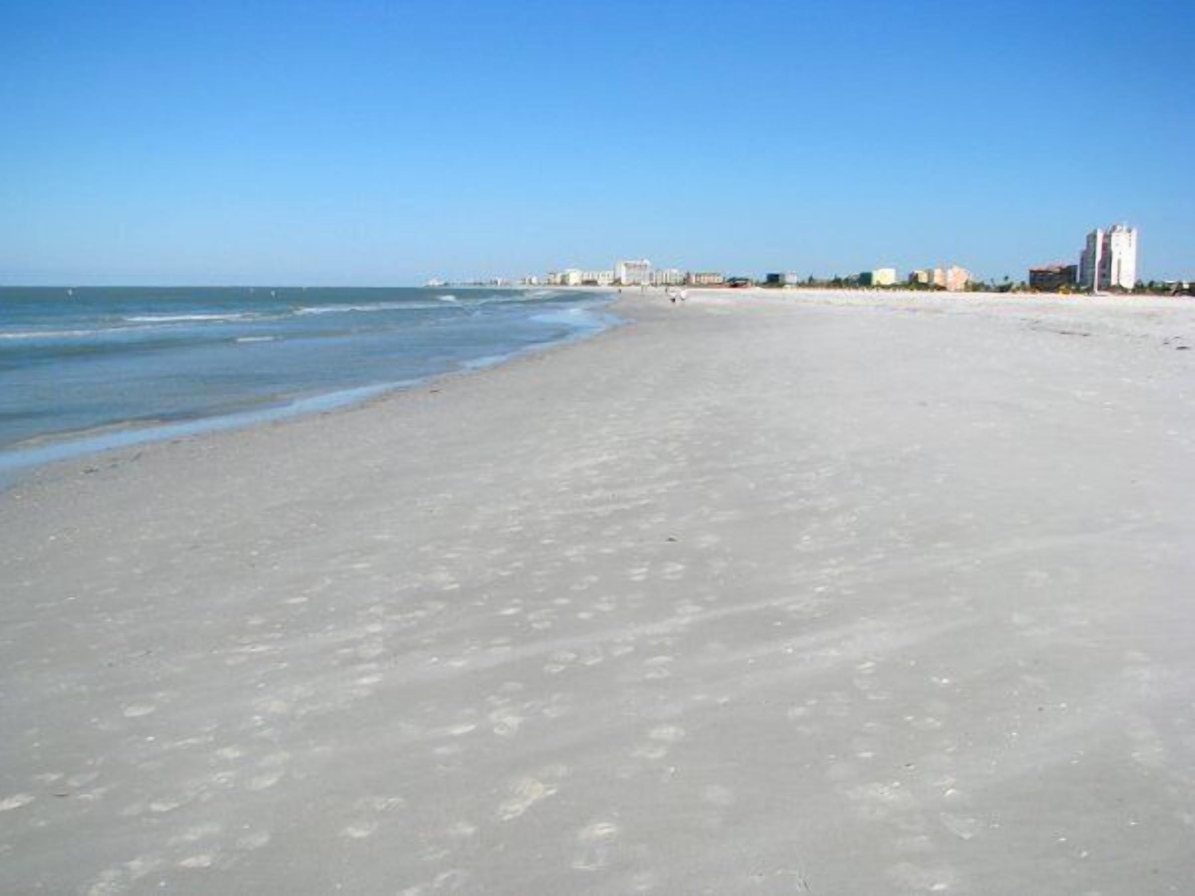 Una extensa playa de arena con cielo azul despejado.