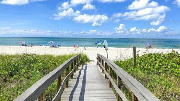 A wooden boardwalk leading to a beach with umbrellas and people.