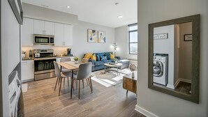 Eine moderne Wohnung mit Küche, Essbereich und Wohnzimmer. Sie beinhaltet einen Esstisch, Stühle, ein Sofa und einen Couchtisch.