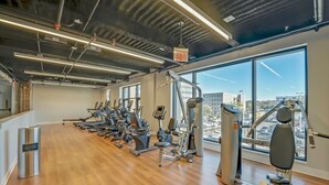 Ein Fitnessstudio mit Cardiogeräten, Krafttrainingsgeräten und Blick auf die Stadt durch große Fenster.
