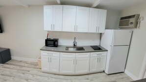 A compact kitchen with white cabinets, a black microwave, a sink, and a white refrigerator. - Satellite Motel - Endless Summer 121 (Treasure Island)