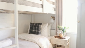 Un lit superposé avec une tête de lit blanche, une table de chevet avec une lampe et une fenêtre avec des rideaux.
