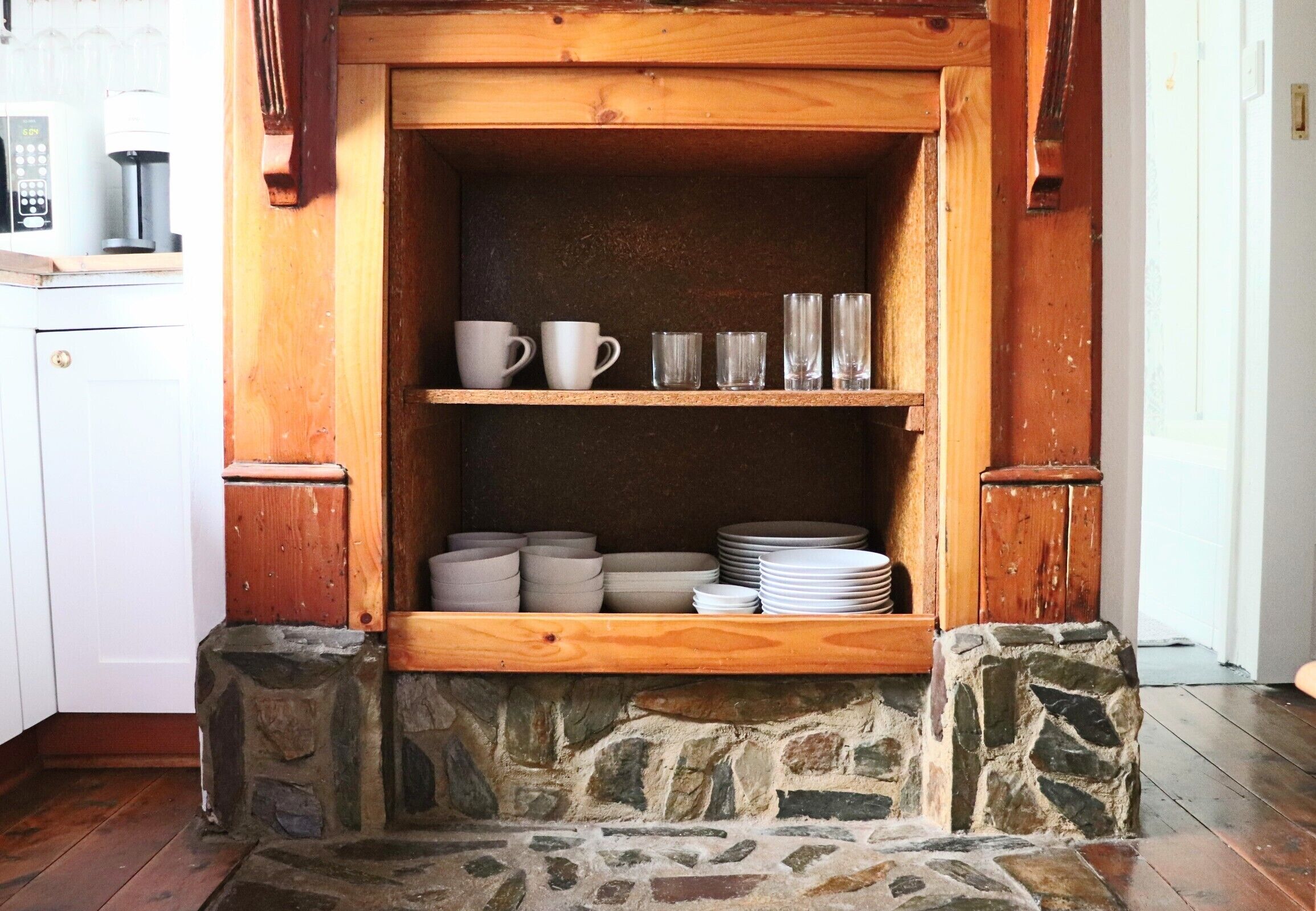 A stone fireplace with shelves above holding cups and plates.
