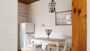 Un coin repas avec une table en bois et des chaises blanches, un réfrigérateur blanc et un luminaire suspendu.