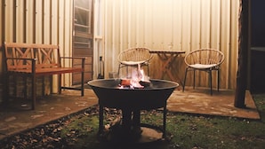 Une terrasse avec un foyer, deux fauteuils en osier et un banc en bois.