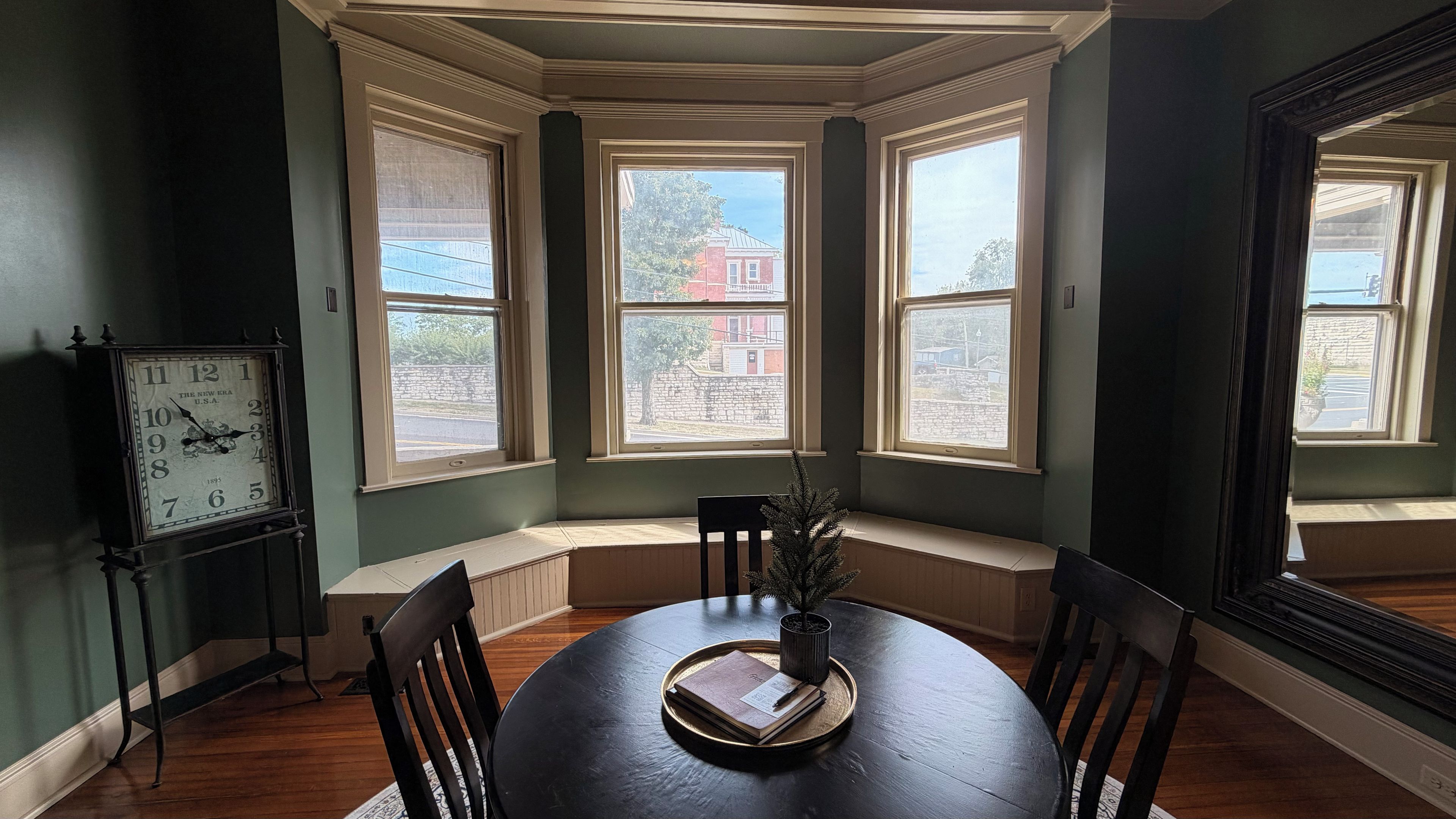 Un comedor con ventanal panorámico, un reloj, una mesa con un libro y una planta.