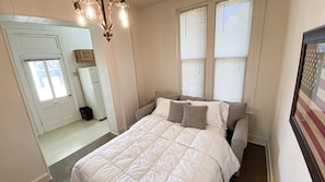 Une chambre à coucher avec un lit, un lustre, une fenêtre avec des stores et une porte.