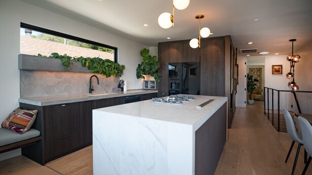 Una cocina moderna con una isla grande, armarios oscuros y vistas al exterior.