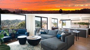 Una sala de estar moderna con un sofá seccional gris, una mesa de centro y vista a un paisaje urbano al atardecer.