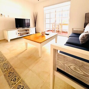 A living room with a television, a coffee table, a sofa, and a window with a view.