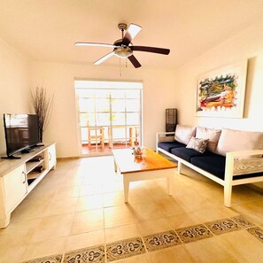 A living room with a television, sofa, coffee table, and a ceiling fan.
