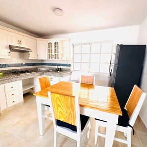 A kitchen with white cabinets, a granite countertop, a black refrigerator, and a wooden dining table with white chairs.