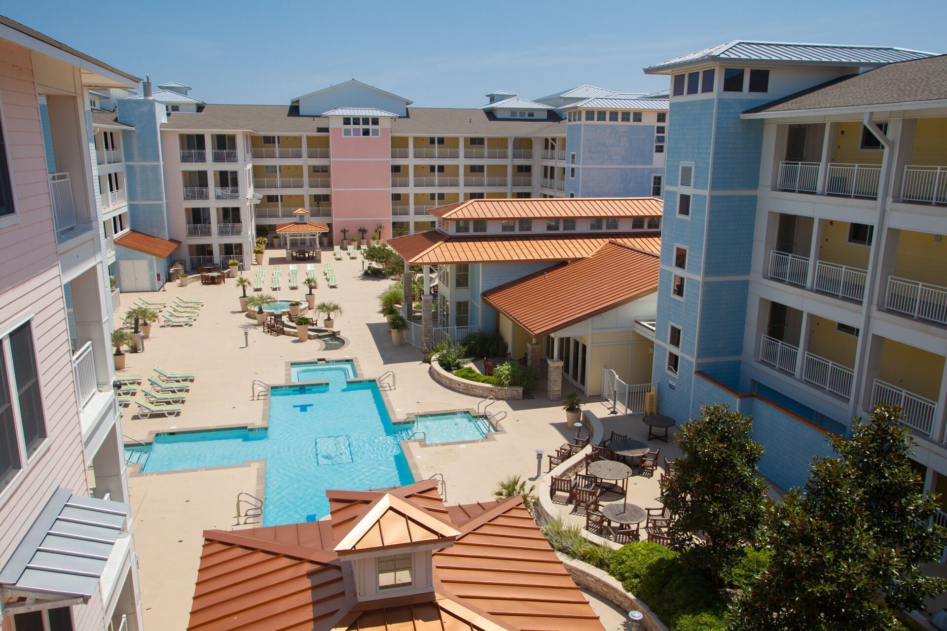A hotel with multiple balconies, a central pool area, and outdoor seating.