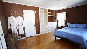 Een slaapkamer met een houten vloer, een bed met blauw beddengoed, een inbouwkast en een deur met een witte handgreep.