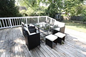 Eine Holzdielen-Terrasse mit einem Tisch mit Glasplatte und vier Stühlen, umgeben von einem weißen Geländer.