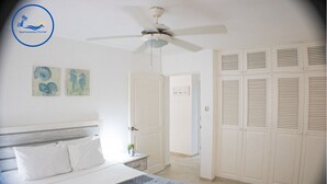 Une chambre à coucher comprenant un lit, un ventilateur de plafond, une table de chevet et une armoire.