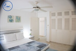 Une chambre à coucher comprenant un lit, un ventilateur de plafond, une table de chevet et une armoire.