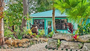 A turquoise building with a glass door, surrounded by a garden with various plants and rocks. - THE RIVER HOUSE, 21 Foot Boston Whaler Included (Jupiter)