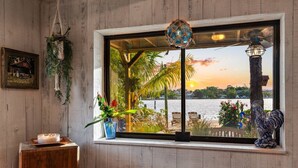 A room with a large window overlooking a beach, wooden walls, a small table with a candle, and decorative items including a hanging light and a sculpture. - THE RIVER HOUSE, 21 Foot Boston Whaler Included (Jupiter)