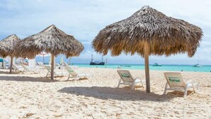 Una playa con sombrillas de paja y sillones blancos.