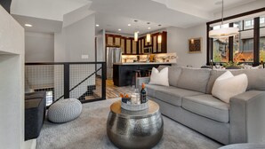 A modern living room with a grey sofa, a round coffee table, and a kitchen in the background. - Central Location, Hot Tub, Chef (Park City)