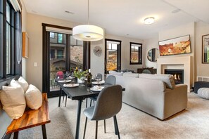 A modern living room with a fireplace, a dining area with a wooden table, and a grey sofa.