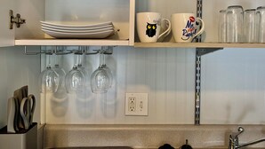 Eine Küche mit weißen Schränken, einer Arbeitsplatte, einem Weinkühlschrank und einem Regal mit Geschirr und Tassen.