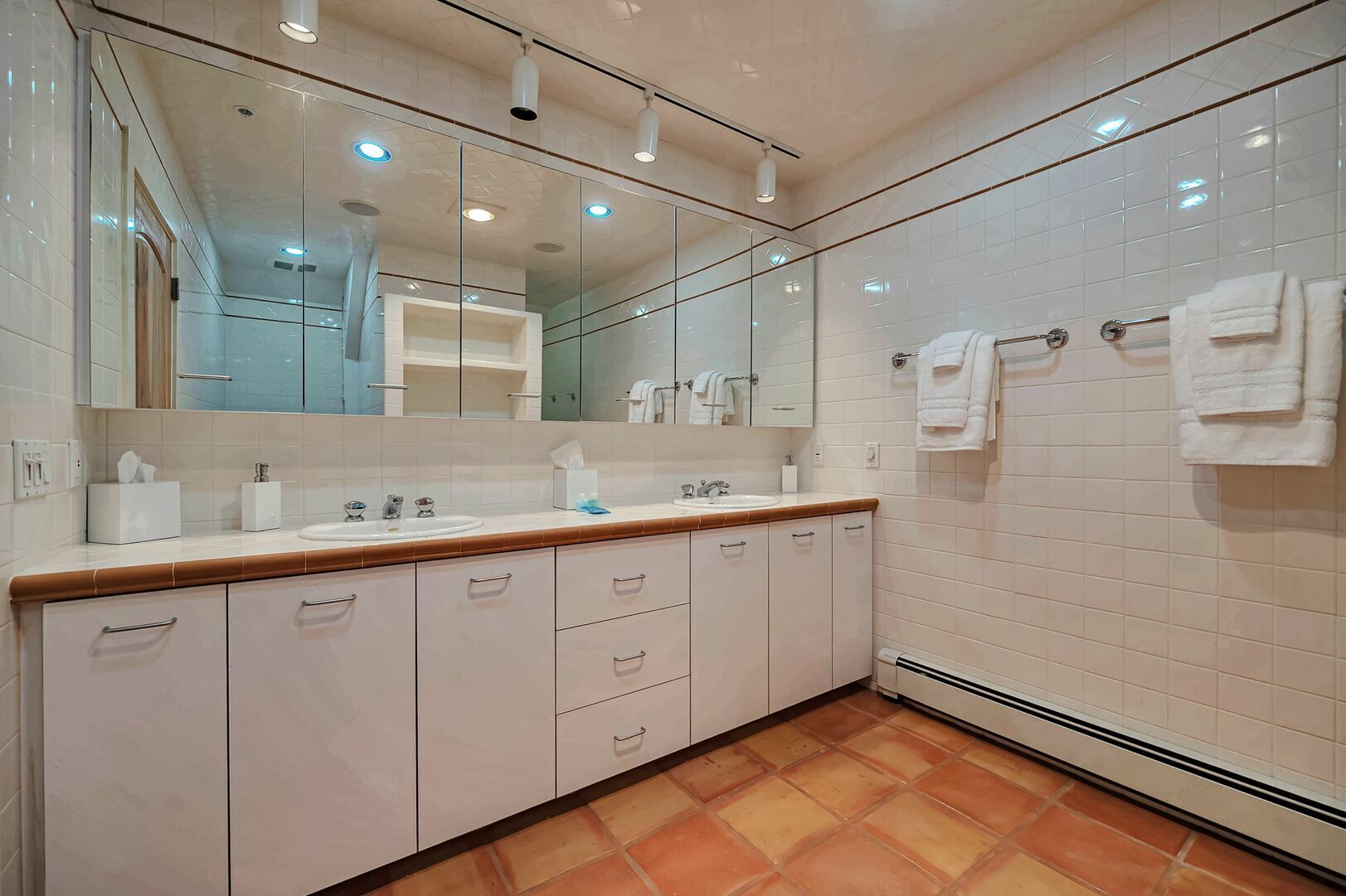 Un bagno moderno con uno specchio grande, piastrelle bianche, un piano d'appoggio in legno e pavimento piastrellato.