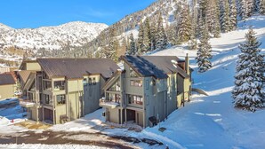 A modern ski resort building with multiple levels and large windows, surrounded by snow-covered mountains and trees. - Ski in/ski out to Alta in this bright, breathtaking new home that sleeps 12 with fireplace! (Alta)