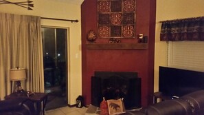 A living room with a fireplace, a sofa, a lamp, and a view of the outdoors. - Bearadise @ The Chalets,  Across from the Ski Lifts !! (Angel Fire)