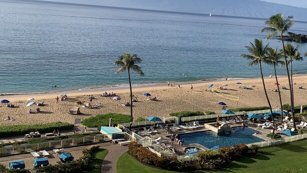 A beach resort with a pool, palm trees, and a view of the ocean and mountains. - Whaler Tower II - 1 Bedroom Condo with Beautiful Ocean View (Lahaina)